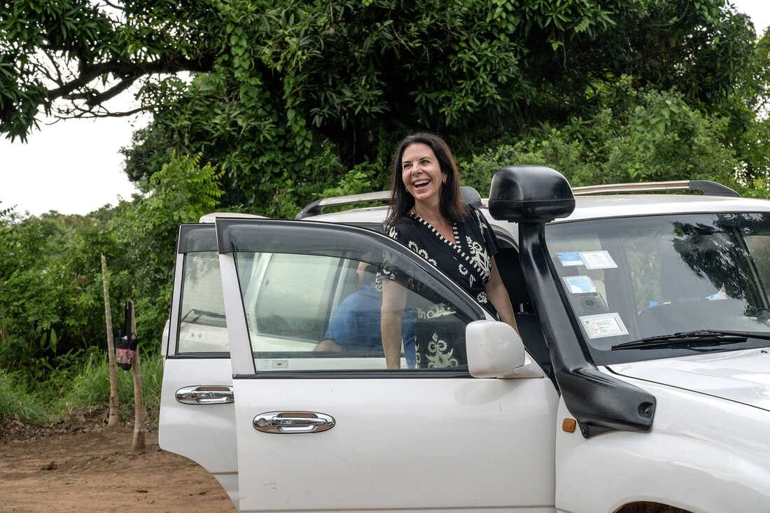 Jodi laughing beside a Land Cruiser under mango trees